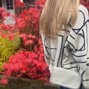 Beige axelväska från Tiamo med kedja - Snygg beige axelväska från Tiamo med silverfärgad kedja och dekorativ kant. Väskan är rektangulär och har ett lock med magnetknäppning samt innerfack med dragkedja. Materialet är mocka och insidan är svart tyg. Perfekt för att lyfta din outfit.