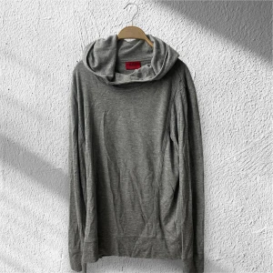 Grå hoodie från Hugo Boss - Säljer en stilren grå hoodie från Hugo Boss med stor huva och långa ärmar. Tröjan är i mjuk bomullsmix och har en clean look utan tryck eller mönster. Perfekt för dig som gillar enkel och snygg streetstyle.