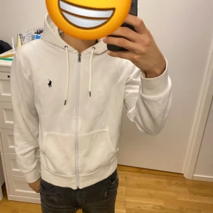 Vit hoodie från Polo Ralph Lauren - Vit hoodie från Polo Ralph Lauren med dragkedja och snörning i huvan. Storlek Medium skick 9,5/10 hör av er för mer info ///