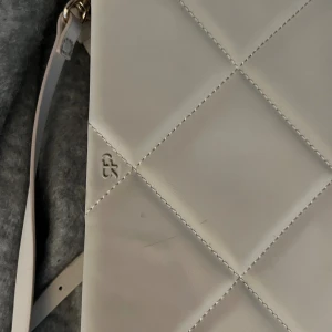 Beige quiltad axelväska ( vet ej märket!!! ) - Snygg beige axelväska  med quiltad design och justerbar axelrem i matchande färg. Väskan har guldfärgade detaljer och ett stilrent, rutmönstrat yttre. Perfekt storlek för mobil, plånbok och småsaker. 