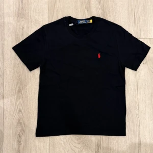 Svart Polo Ralph lauren T-shirt  - En snygg och simple svart polo ralph lauren T-shirt. Den röda loggan är liten men får T-shirten att sticka ut på ett unikt sätt. Topp kvalité, rimligt pris och postar inom kort.