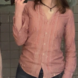 Randig röd- och vit skjorta - Säljer en snygg randig skjorta i rött och vitt med v-ringning. Den är figursydd. 