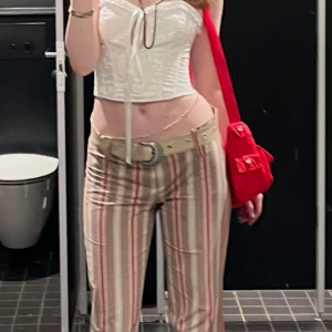 Lowwaist randiga kostymbyxor - Lowwaist röd-beige randiga kostymbyxor.är 172 och lite över anklarna på mig. OBS: Bältet ingår inte. Kan även tillägga att korsetten i bilden också är öppen för försäljning: 199 kr