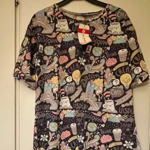 *NY*Färgglad T-shirt  från Bigdart i stl 38/40, Presenttips  - Ny tunn skön lite längre t-shirt med slits på båda sidor, fr Big Dart, Turkiet.  Normal i storleken.  Med ett unikt och färgglatt mönster. Motivet består av en mängd olika figurer och symboler som datorer, kaffekoppar, jordglobar och pratbubblor med ord som 'Chat', 'Inspire', 'Discover' och 'Dream'. T-shirten har rund hals, korta ärmar och är gjord i mjuk polyester. 