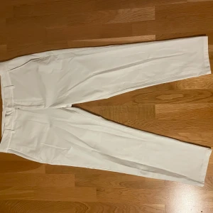 Vita kostymbyxor från Zara - Snygga vita kostymbyxor från Zara med raka ben och klassisk passform. Byxorna har hällor för bälte, diskreta sidofickor och bakfickor med knapp. Perfekta för en clean och stilren look. Materialet känns mjukt och lätt.