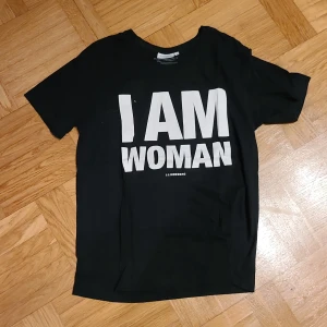 T-shirt - Svart t-shirt med texten I am woman från J. Lindesberg. 
