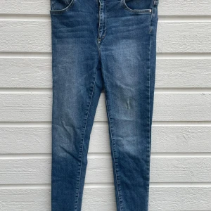 Blå skinny jeans från Never Demin  - Det Snygga blå jeans med stretch från Never Demin i storlek M. Modellen är skinny med hög midja och croppade ben med rå, fransad kant. Klassisk femficksdesign och dragkedja med knapp framtill. Perfekta för dig som gillar en smal siluett och trendiga detaljer.