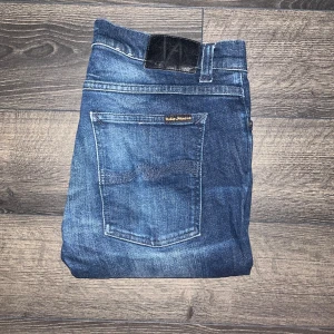 Nudie Jeans Tight Terry  - Snygga mörkblå jeans från Nudie Jeans, modellen Tight Terry. femficksdesign och subtila slitningar. Materialet är mestadels bomull med lite elastan för extra stretch. Perfekt för dig som gillar en tajt siluett. Midja43cm, längd 103cm. JAG SKICKAR EJ FLER BILDER NÄR JAG BÄR JEANSEN! för storleksguide hänvisar jag till måtten och för bättre inblick i passformen rekommenderar jag att googla på modellnamnet :) s3