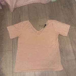 Beige v-ringad topp med korsdetalj - Säljer en beige topp med korta ärmar och snygg v-ringning framtill. Toppen har en korslagd detalj vid halsen som ger en extra touch. Tillverkad i mjukt material, perfekt för en chill och stilren look.