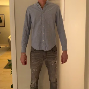 Blå oxfordskjorta från Pull&Bear - Klassisk ljusblå oxfordskjorta från Pull&Bear i 100% bomull. Skjortan har button down-krage, vita knappar och lång ärm. Perfekt för en clean och stilren look.