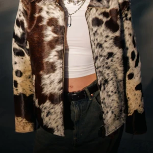 Brun och vit pälsjacka med dragkedja - Säljer en unik pälsjacka med coolt ko-inspirerat mönster i brunt, vitt och svart. Jackan har klassisk krage, rak passform och stängs med dragkedja framtill. Perfekt statement-plagg för dig som vill sticka ut.