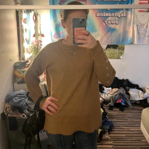 Beige stickad tröja med rund hals - Mysig beige stickad tröja med rund halsringning och ribbade muddar vid ärmslut och nederkant. Långärmad och loose fit, perfekt för lager-på-lager och chill dagar. Enkel att matcha med jeans eller kjol för en avslappnad look.