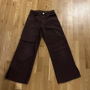 Bruna wide high waist byxor H&M - Snygga bruna byxor från H&M med wide fit och hög midja. Modellen har justerbar midja, klassiska fickor fram och bak samt raka ben med bred siluett. Perfekta för dig som gillar en avslappnad och trendig look.