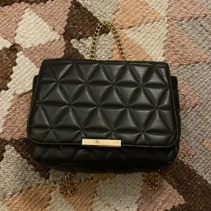 Svart väska med gulddetalj - Snygg axelväska med knäppe. Perfekt till shoppingturen eller till en vanlig tröja. Köpt på glitter