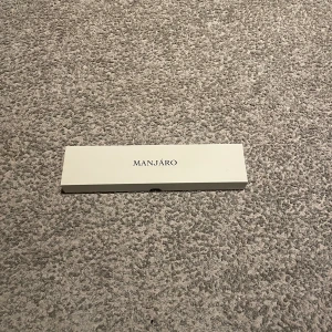 Klocka - En stilren klocka för dig som vill vara lite diskret samt ha en snygg klocka. Det är ett brun/beige armband med små guld detaljer och en urtavla som är vit med en lite palm. Använd 1 gång. Skick 9/10