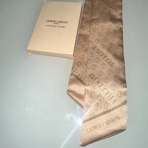 Beige silkeshalsduk från Giorgio Armani scarf  - Snygg beige halsduk/scarf/hår accessoar/ Väsk accessoar från Giorgio Armani i glansigt silkesmaterial. Perfekt accessoar för att lyfta din outfit. Cirka 40cm lång & 3 cm bred. ✨🎁