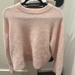 Ljusrosa stickad tröja Gina Tricot  - Mysig ljusrosa stickad tröja från Gina Tricot med rund hals och ribbade muddar vid ärmslut och nederkant. Perfekt för dig som gillar en enkel och soft look. Tröjan har lång ärm och är i ett fluffigt material som känns skönt mot huden.