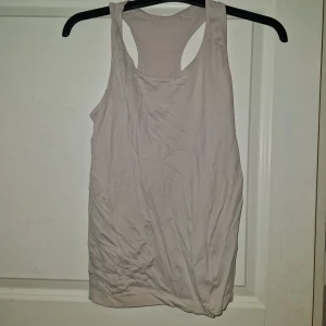 Ljusgrå ärmlös linnetopp - En enkel och stilren ljusgrå linnetopp med brottarrygg. Perfekt för varma dagar eller som lager under en skjorta. Tillverkad i mjuk bomull som känns skön mot huden. Passformen är normal och toppen är helt utan ärmar.