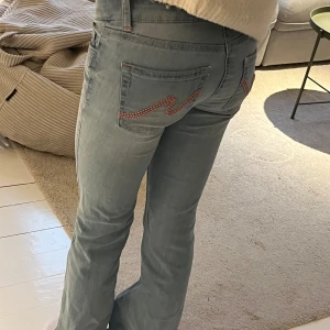 Ljusblå bootcut jeans från Nelly - Snygga ljusblå jeans från Nelly med bootcut passform och klassisk femficksdesign. Jeansen har rosa broderade detaljer på bakfickorna och dubbla knappar i midjan. 