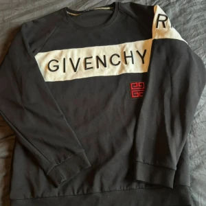 Svart sweatshirt från Givenchy - Säljer en svart sweatshirt från Givenchy med vit panel och stor logga framtill. Tröjan har långa ärmar, rund halsringning och en röd broderad detalj på bröstet. Tillverkad i mjuk bomull, perfekt för en stilren och trendig look. Äkta självklart 