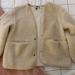 Beige teddyjacka från H&M - Säljer en snygg jacka från H&M. Används helst under våren/sommaren/början av hösten. 💕 Vanlig insida, blir varm av utsidan. Fickor på båda sidorna. Stängs med knappar, samma med fickorna.