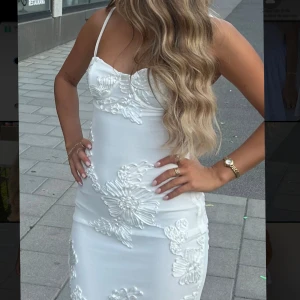 Vit långklänning med blommig spets - Säljer denna fina mottagningsklänning som är slutsåld i alla storlekar köpte den för 1600kr inkl frakt den är Supersnygg vit långklänning med tunna axelband och figurnära passform. Klänningen har broderade blommor i spets över hela tyget och en lätt v-ringad byst. Perfekt för dig som vill sticka ut med en elegant och feminin look. 