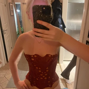 Röd spetskorsett från PrettyLittleThing - Säljer en röd korsett från PrettyLittleThing! Den är i stl 8. Men eftersom att den har snörning i ryggen så passar den väldigt många. Den är i färgen brunt orange. Aldrig använd, endast testad. 