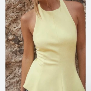 Gul peplum topp med halterneck - Snygg ljusgul halterneck topp med peplum och markerad midja. Toppen är ärmlös och har öppen rygg med knäppning i nacken. Helt ny aldrig använd med prislapp kvar, endast testad💖