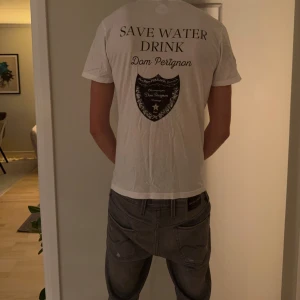 Vit Dom Perignon t-shirt från NAKD - Säljer en vit t-shirt från NAKD med trycket 'SAVE WATER DRINK Dom Perignon' och en stor svart Dom Perignon-logga på ryggen. T-shirten är kortärmad, har rund hals och är gjord i mjuk bomull. Perfekt statement-plagg för dig som gillar coola prints.