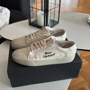 Saint Laurent ysl sneakers - Väldigt feta skor från Saint Laurent med handskriven logga på sidan. Skorna har rund tå, platt sula och snörning. Tillverkade i canvas med detaljer i skinn och guldtext på plösen. Perfekt för dig som gillar minimalistisk och stilren design.