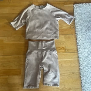 Beige ribbade träningsshorts Stronger - Säljer ett par beige ribbade träningsshorts från Stronger med hög midja och diskret logga på linningen. Materialet är stretchigt och består av 94% polyamid och 6% elastan, vilket gör dem perfekta för gymmet eller annan träning. Snygg, slim passform och stilren design.