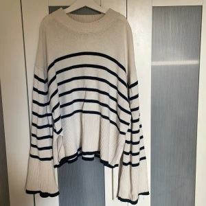 Randig stickad tröja Gina Tricot - Säljer en vit och svart stickad tröja från Gina Tricot i storlek S. Tröjan har breda, långa ärmar  och ribbade muddar, samt ett snyggt randigt mönster. Passformen är loose och den har en rund halsringning. Perfekt för dig som gillar chill och trendig stil.
