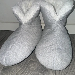 Grå fluffiga toffelboots - Mysiga grå toffelboots med fluffigt vitt foder på insidan. Gjorda i mjuk polyester och har en rund tå. Står inte vad för storlek det är, men passar 38-40. Bra att ha på när det börjar bli kallare.