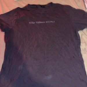 Svart t-shirt med tryck XXL - Svart t-shirt i storlek XXL med texten 'KEEP THINGS SIMPLE' tryckt på bröstet. Klassisk rund hals och korta ärmar. Mjuk och skön känsla, perfekt för chill dagar. Materialet känns som bomull och passformen är normal.