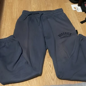 Mörkblå mjukisbyxor från Hoodrich M - Mörkgrå mjukisbyxor från Hoodrich med tryckt logga på ena benet. Byxorna har elastisk midja med snörning och muddar vid bensluten. Tillverkade i mjukt material för maximal komfort, perfekta för chill eller streetwear.