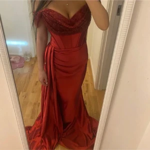 Bal/fest paket - Säljer detta bal/fest paket som innehåller klänning, smycken, klackar och väska. Snygg vinröd långklänning i glansigt satin material med axelbandslös design och paljetter över bysten och ärmarna. Klänningen har en elegant drapering (korsett) framtill och stängs med dragkedja i ryggen. Jag har sytt upp den så den passar perfekt för dig som är 160-165 cm lång. Jag har även kvar delen som jag sytt bort om man är lite längre och vill lägga till det. Fri frakt kan lösas. Endast använda 1 gång.