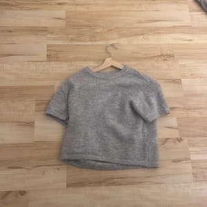 Grå stickad tröja Gina Tricot - Mysig grå stickad tröja från Gina Tricot med korta ärmar och rund hals. Tröjan har en enkel, clean look och är lite längre baktill. Perfekt för dig som gillar en chill och stilren vibe.
