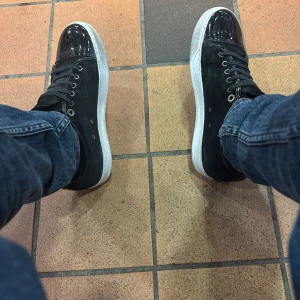 Lanvins - Svarta sneakers med vit sula och snörning. Tåpartiet är i blankt lackmaterial som ger en cool kontrast mot resten av skon som är i mocka. Rund tå och metallfärgade öljetter för snören. Perfekt för dig som gillar stilrena och moderna detaljer.