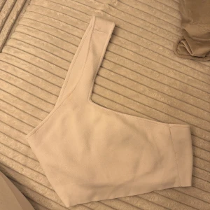 Beige oneshoulder topp från Zara - Säljer en stilren beige oneshoulder topp från Zara i storlek M. Toppen har en asymmetrisk design med en axel och är tillverkad i mjukt, stickat material som ger en skön känsla. Perfekt för dig som gillar minimalistisk och trendig stil.