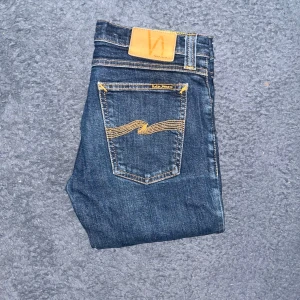 Nudie Jeans  - Snygga mörkblå jeans från Nudie Jeans, modellen Tight Long John. Jeansen är slim fit med skinny passform och tillverkade i stretchig denim av bomull och lycra. Midja 38cm, längd 105cm.  Ifall det inte finns någon bild i annonsen där jag bär plaggen jag säljer så är det för att jag ej kan ha storleken heller passformen, så kolla måtten för storlek och googla på modellnamnet för passform 😉42