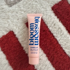 Bloom & Blossom handkräm 15ml - Handkräm i en ljusrosa tub med blå text från Bloom & Blossom. Innehåller niacinamid som hjälper till att förbättra hudens utseende. Tuben rymmer 15 ml och är smidig att ha med i väskan. Perfekt för att hålla händerna mjuka och återfuktade.