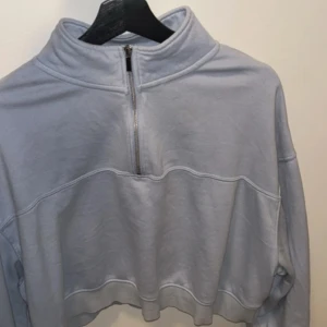 Ljusblå croppad half zip hoodie - Säljer en ljusblå croppad hoodie från Bik Bok med half zip-dragkedja och hög krage. Tröjan har långa ärmar och är tillverkad i mjuk bomullsmix, perfekt för chill dagar. Enkel och stilren design som är lätt att matcha med jeans eller leggings.