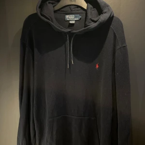 Mörkblå hoodie från Polo Ralph Lauren - Svart hoodie från Polo Ralph Lauren med klassisk röd logobrodyr på bröstet. Tröjan har huva, stor är tillverkad i mjuk 100% bomull. Perfekt för chill dagar och streetwear-stil.