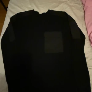 Svart långärmad klänning Mos Mosh - Svart långärmad klänning från Mos Mosh med enkel design och rund hals. Klänningen har en diskret bröstficka och är tillverkad i ett mjukt material som känns skönt mot huden. Perfekt för dig som gillar stilrena och minimalistiska plagg.