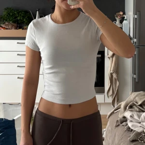 Vit croppad t-shirt med kort ärm - Säljer en enkel och fräsch vit croppad t-shirt med rund hals och korta ärmar. Toppen har en tight passform och är tillverkad i mjuk bomull som sitter skönt mot kroppen. Perfekt att styla med jeans eller mjukisbyxor för en chill look.