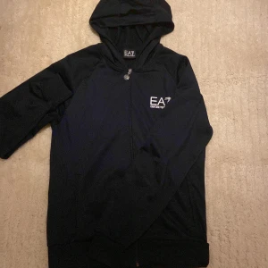 Mörkblå hoodie med dip EA7 Emporio Armani - Mörkblått EA7 Armani zip hoodie. Använt fåtal gånger, skicken är nästan hel ny. Skulle passa du som är 170-180 helt perfekt. Färgen ser ut som svart men ör mörkblå. Ser riktigt fet ut i riktiga livet! 