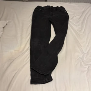 Svarta jeansbyxor från 157 - Svarta jeansbyxor från 157 med klassisk femficksdesign och silverfärgade knappar. Byxorna har rak passform och normal midja, tillverkade i slitstarkt jeanstyg. Perfekt för dig som gillar en enkel och stilren look.