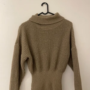 Beige stickad poloklänning - Mysig beige stickad klänning med polokrage och lång ärm. Klänningen har en markerad midja och grovstickad struktur upptill som övergår i en smalare stickning nedtill. Perfekt för kyliga dagar och enkel att styla med boots eller sneakers.