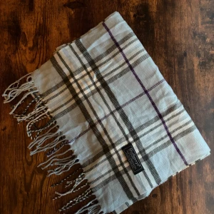 Burberry halsduk - Klassisk Burberrys-halsduk i 100% lammull, tillverkad i England. Mjukt och varmt material i ikoniskt rutmönster. Passar både dam och herr. I mycket bra skick små fläckar eller utan hål – perfekt för höst och vinter. 