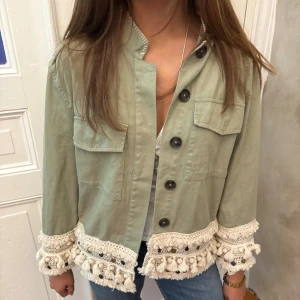 Grön jeansjacka med virkade detaljer - Snygg ljusgrön overshirt med stora svarta knappar och två bröstfickor. Jackan har unika virkade och fransade detaljer i beige med bollar längs nederkant och ärmslut. Perfekt för dig som vill sticka ut med en boho-vibe och gillar coola detaljer‼️. OBS KAN POSTA TIDIGAST 24/11‼️